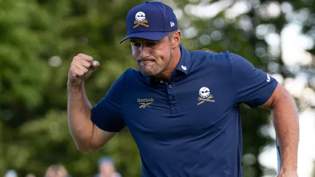 Bryson DeChambeau celebra con el puño cerrado en un campo de golf, vestido con polo azul marino y gorra con calavera.
