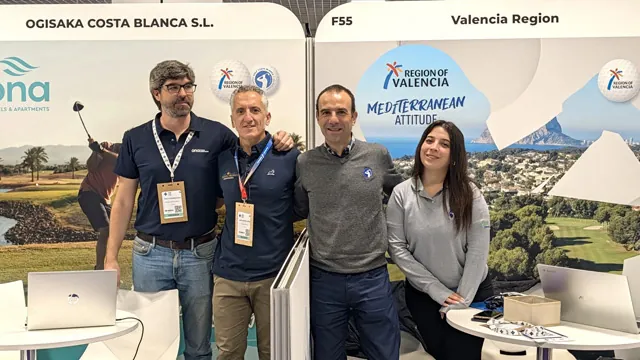 Cuatro personas posan en un stand de la Region of Valencia en una feria, con paneles de campos de golf y la costa al fondo