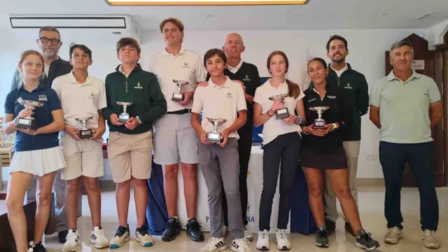 Grupo de jóvenes golfistas y adultos posando con trofeos de premio en un salón, con un cartel azul de fondo.