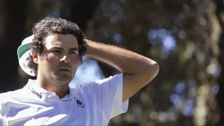 Golfista con polo blanco y gorra verde y blanca, con la mano en la cabeza, mirando a un lado entre árboles desenfocados