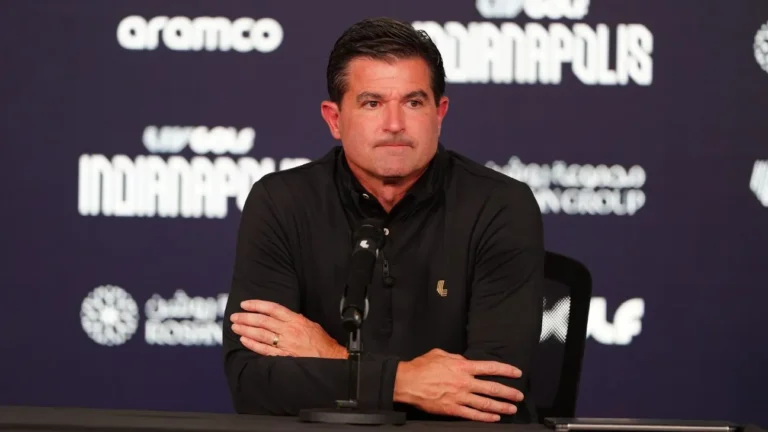 Hombre con camisa negra y brazos cruzados, sentado ante un micrófono en una rueda de prensa de LIV Golf Indianapolis.