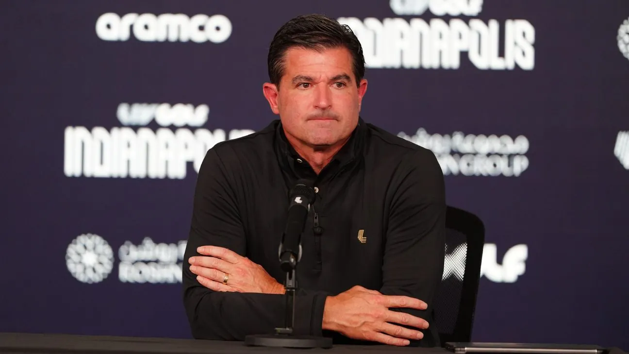 Hombre con camisa negra y brazos cruzados, sentado ante un micrófono en una rueda de prensa de LIV Golf Indianapolis.