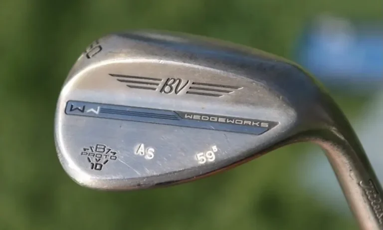 Cabeza de un wedge de golf plateado de 59 grados, con grabado BV Wedgeworks, sobre un fondo de hierba verde desenfocada.