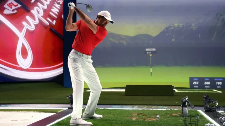 Golfista con polo rojo y gorra blanca lanza un swing con driver en un simulador con pantalla de montañas