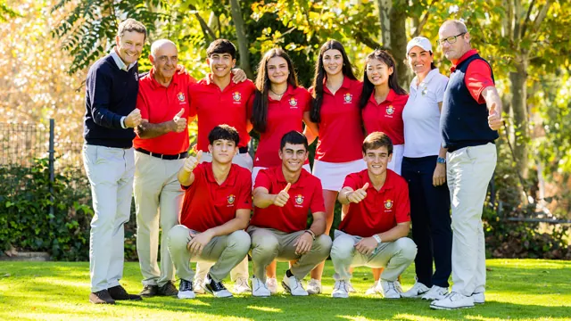 Grupo de golfistas con polos rojos posando sonrientes en un campo de hierba, con árboles al fondo
