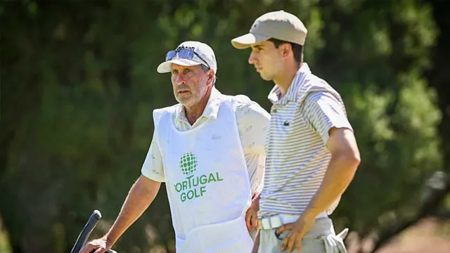 Dos hombres en un campo de golf: un caddie mayor con gorra y peto blanco de Portugal Golf, y un joven con polo a rayas.