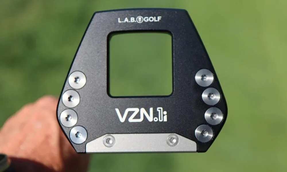 Putter negro L.A.B. Golf VZN.1i de cara mallet con pesos plateados, sujetado en la mano sobre un fondo verde de hierba