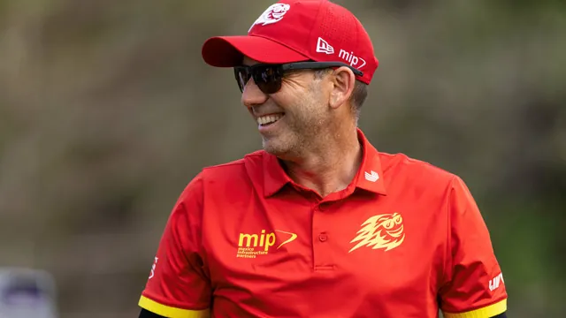Hombre sonriente con gorra roja, gafas de sol y polo rojo con logo de mip, al aire libre con fondo verde desenfocado.